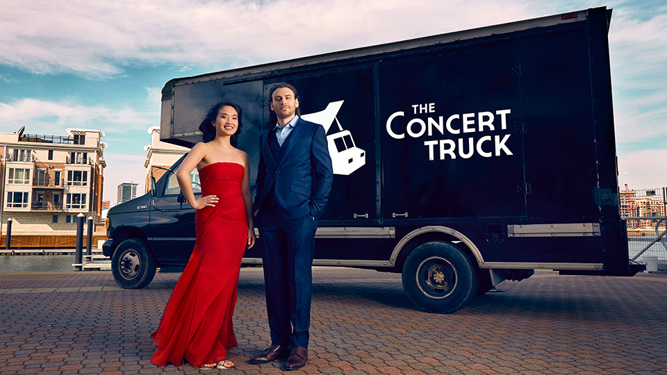 a woman in a red dress and a man in a suit stand in front of a black truck with the words the concert truck on it