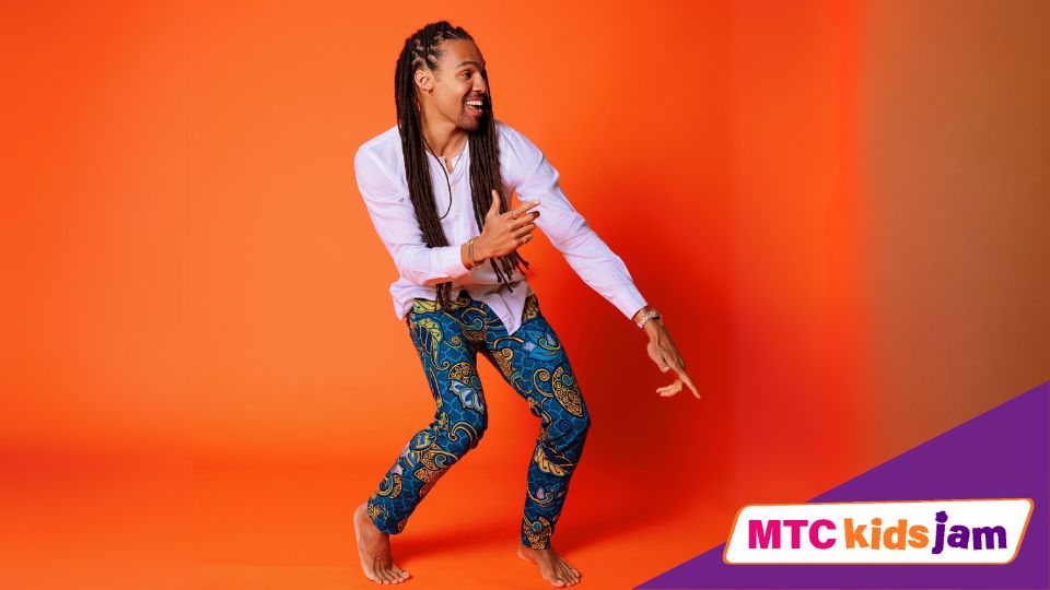 Pierce Freelon smiles and dances in front of a bright orange background.