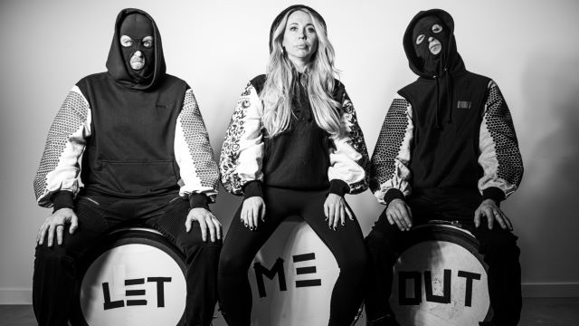 black and white photo of three musicians sitting on drums that say Let Me Out