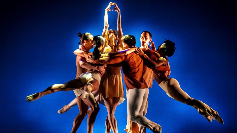 a group of dancers form a tight circle while standing under a blue spotlight