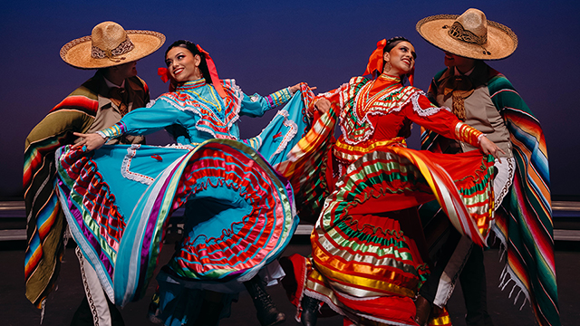 dancers in traditional dress twirl their colorful skirts