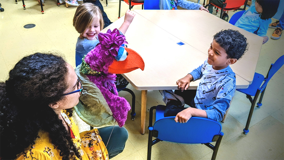 Two smiling children work with a puppeteer at a classroom workshop