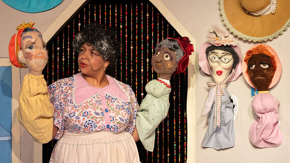 A woman performing a puppet show holds up two puppets