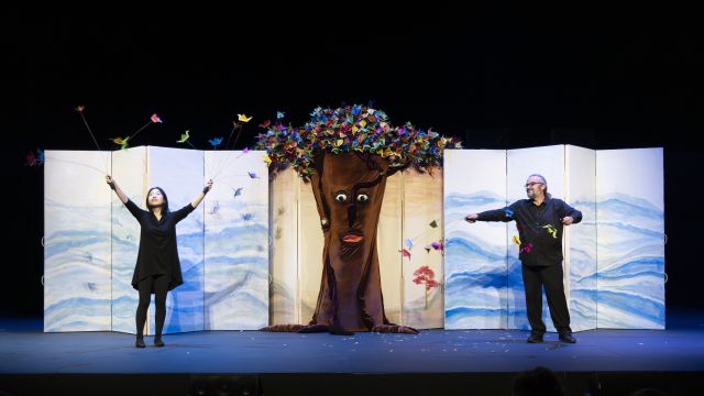two actors on stage on either side of a tree that has origami cranes instead of leaves
