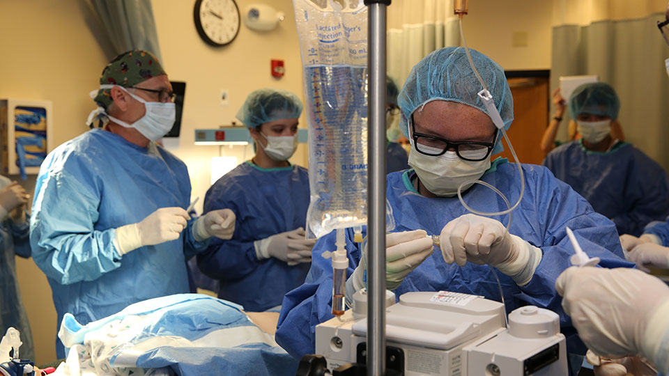 A person connects an IV tube to a monitor in an operating room