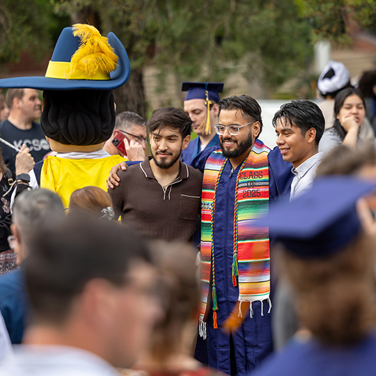 Student in cap and gown posing with parents on either side