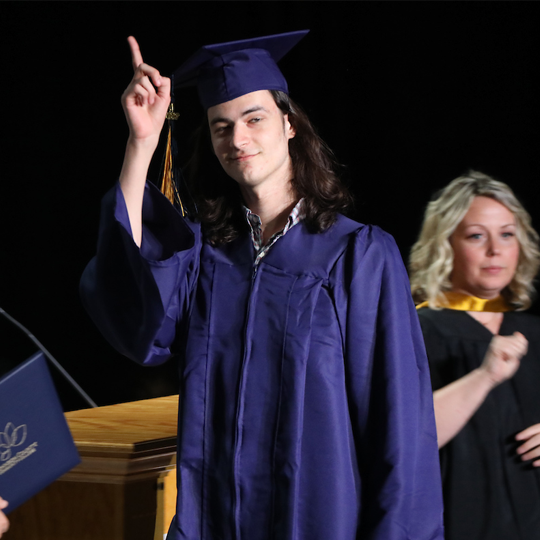 A graduate walking across the stage holding up the number 1 gesture