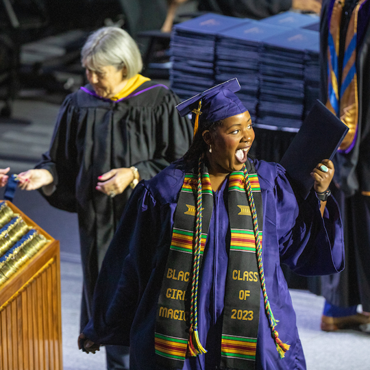 Graduate wearing a stole waving and grinning at attendees
