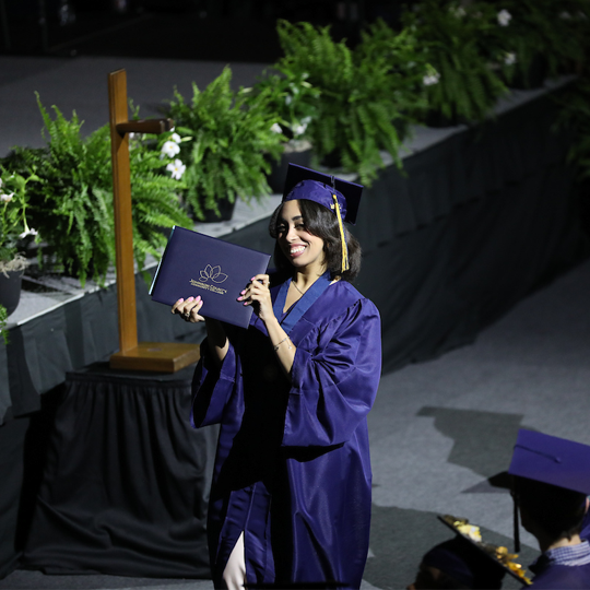 Graduate walking across holding up her diploma