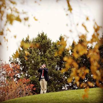 Student veteran playing taps on a bugle surround by fall foliage