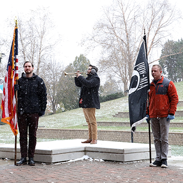 Flag bearers on either side of a student veteran bugler; snow is falling