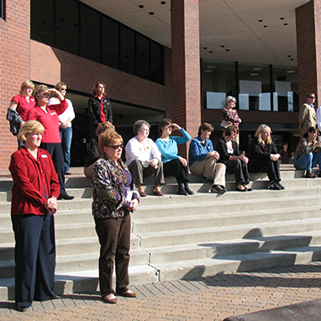 People sitting on the steps of the COMS building listening to Taps