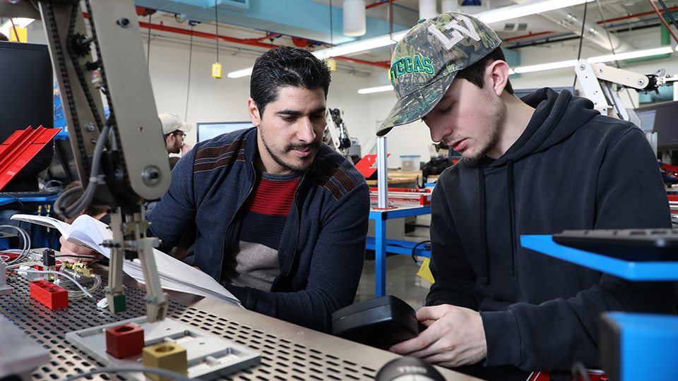 two jccc students sitting at a desk in a lab working on a project