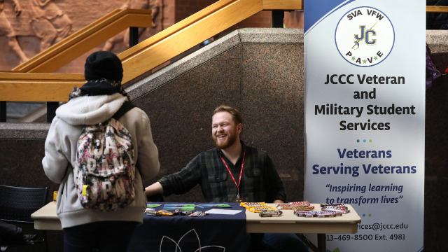 Student representating the veteran and military resource center is at a table speaking to another student.