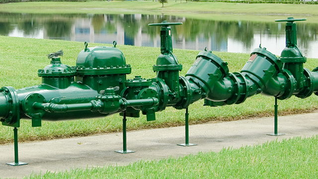 a green backflow device is installed next to a small pond.