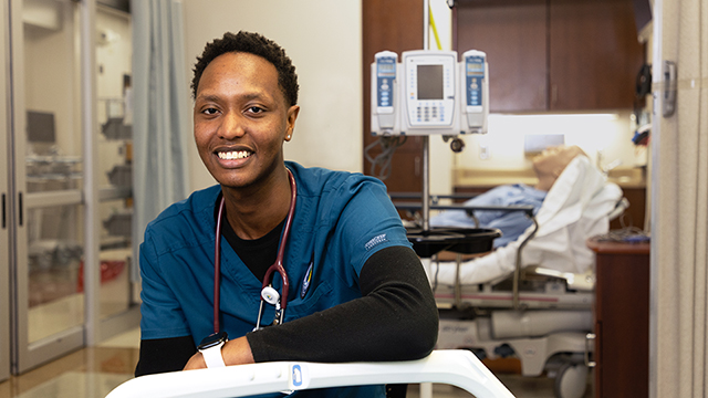Ian Kibet, wearing scrubs, sitting in the simulation lab